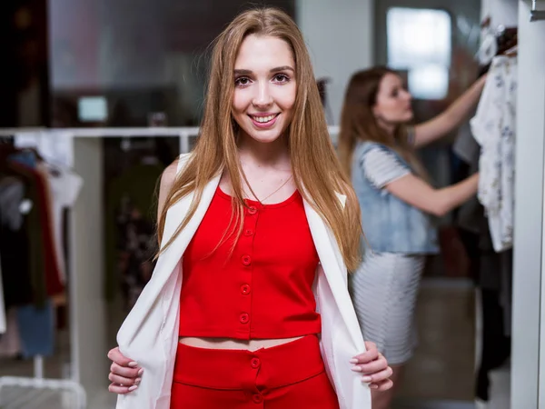 Retrato de una joven modelo femenina que mira en el espejo vistiendo top rojo y conjunto de coord falda y chaleco largo de pie en una sala de exposición — Foto de Stock