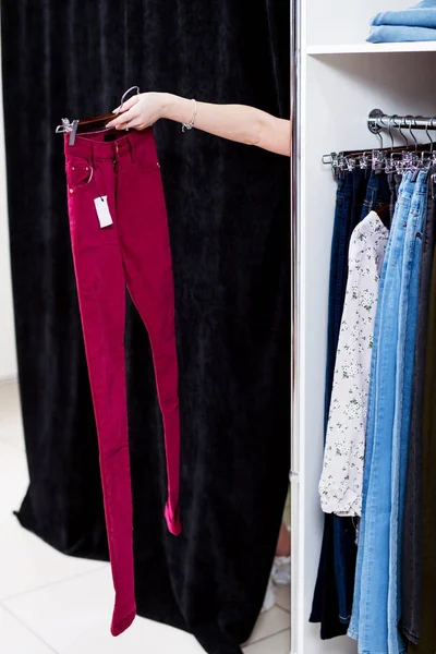 Žena se snaží na kalhoty v obchodě s oděvy natáhl ruku z vybavení pokoje drží kalhoty — Stock fotografie