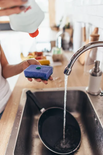 Женщина кладет моющее средство в губку, чтобы вымыть кастрюлю в раковине на кухне. Посуда для мытья рук. Крупный план . — стоковое фото