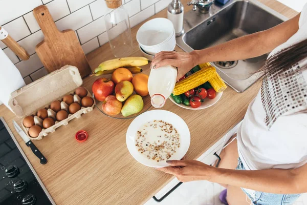 Vrouw gieten melk in plaat met eiken vlokken. — Stockfoto