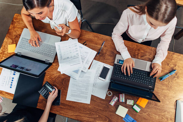 Top view of three women working with documents using laptops sitting at desk