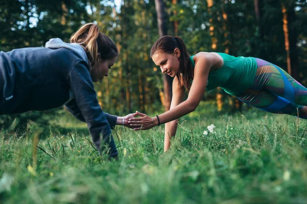 Дві дівчини роблять друзі тренування на відкритому повітрі, виконуючи штовхання, щоб ковзати по траві — стокове фото