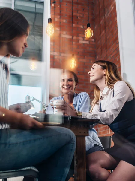 Tre glada kvinnor dricka kaffe, chattar och skvallra i office — Stockfoto