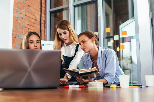 Birlikte bir çalışma odası masasında oturan laptop ve ders notları kullanarak ödev üç kadın üniversite öğrencileri — Stok fotoğraf