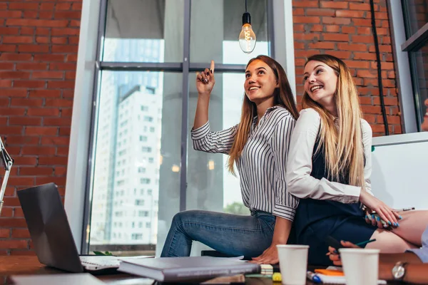 Studenten zitten samen op Bureau in de klas, een meisje wijzend op de gloeilamp als het hebben van een briljant idee. — Stockfoto