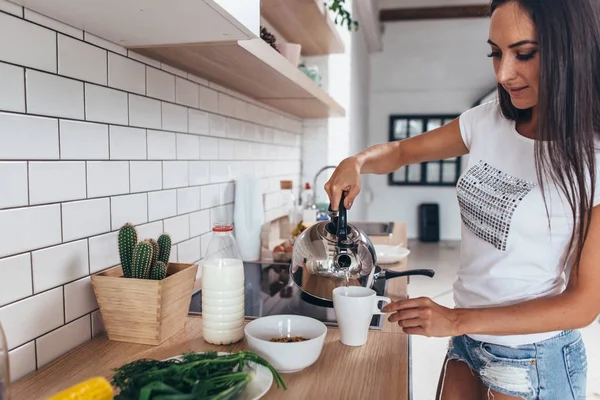 Vrouw gieten van kokend water in een beker uit de waterkoker. — Stockfoto