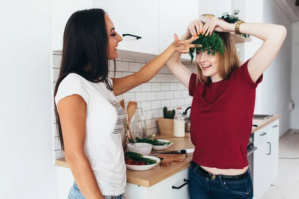 Las mujeres en la cocina bromean, se ríen y se divierten. Jugando con verduras —  Fotos de Stock