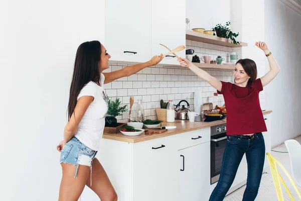 Two woman image that they are fighting on swords by wooden spatulas in kitchen — Stock Photo, Image