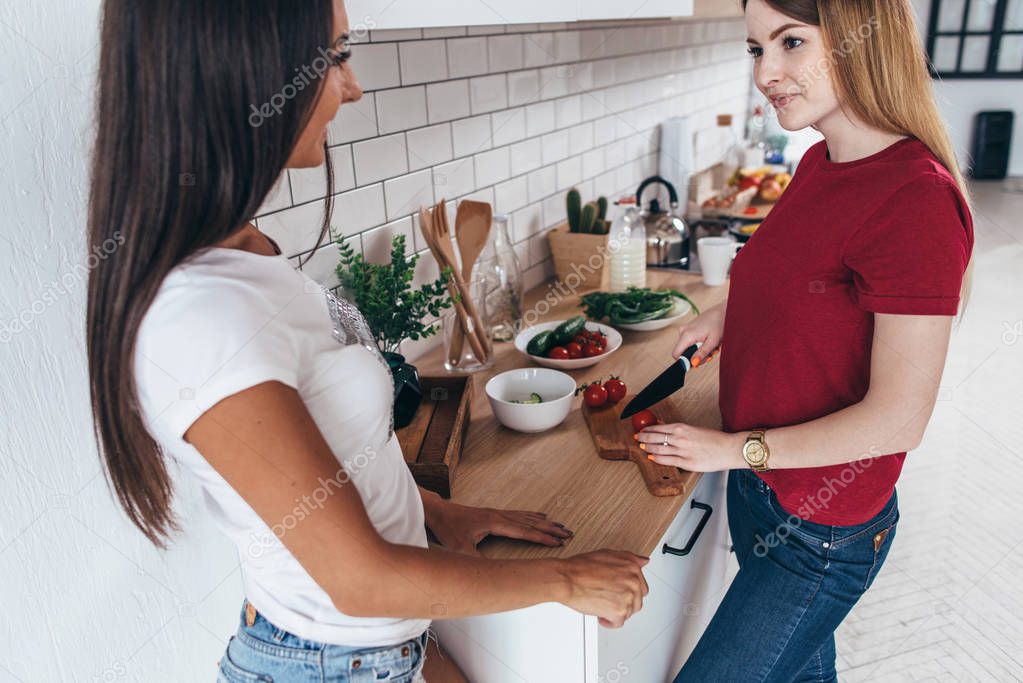 Female friends in kitchen preparing together salad ...