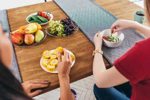 Freunde sitzen am Tisch, reden und essen Gemüse an der Hand. — Stockfoto