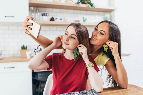 Přátelé v kuchyni hraje, pořizování selfie pomocí ovoce jako jsou náušnice. — Stock fotografie