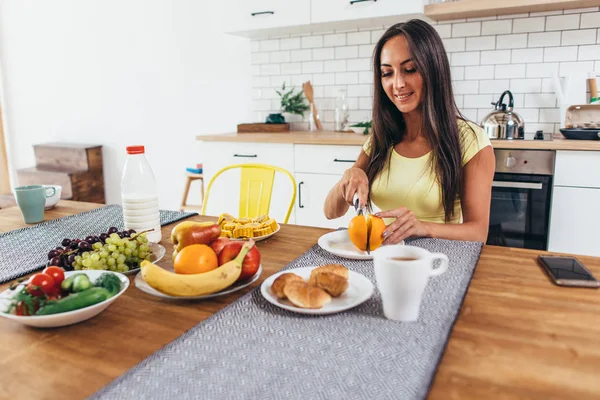 Breakfast with fruits, orange, coffee and croissant. Woman sitting at kitchen table — Stock Photo, Image