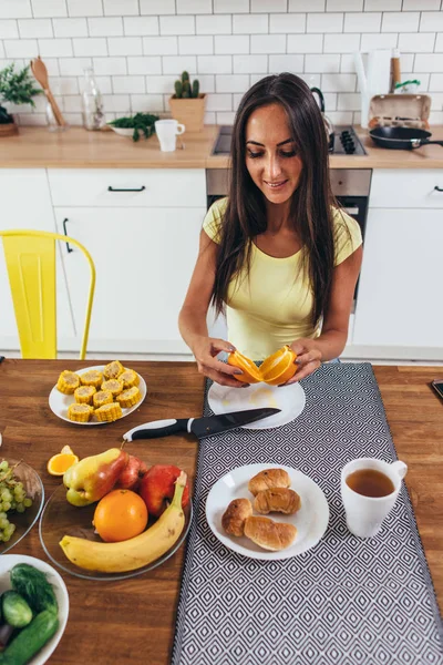 Kadın yemek yerken, portakal yeme mutfak masasında. — Stok fotoğraf
