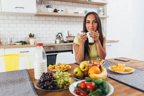 Ung kvinna dricker kaffe på köket på morgonen tittar på kameran. — Stockfoto