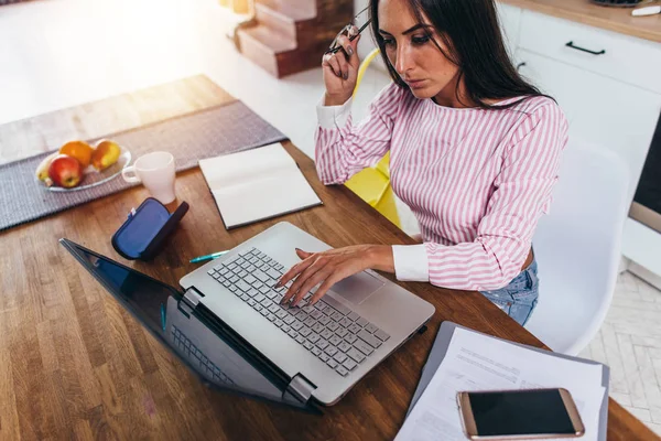 Donna che utilizza il computer portatile mentre seduto in cucina e lavorare sul computer portatile . — Foto Stock