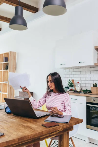 Egen företagare kvinna tittar på dokument och använder bärbar dator för arbete — Stockfoto