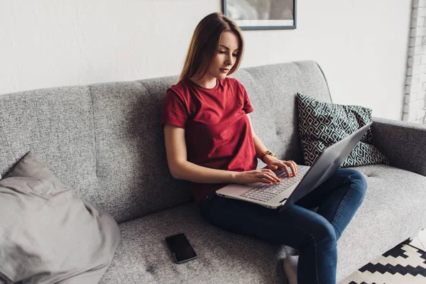 Młoda kobieta za pomocą laptopa w domu siedzi na kanapie — Zdjęcie stockowe