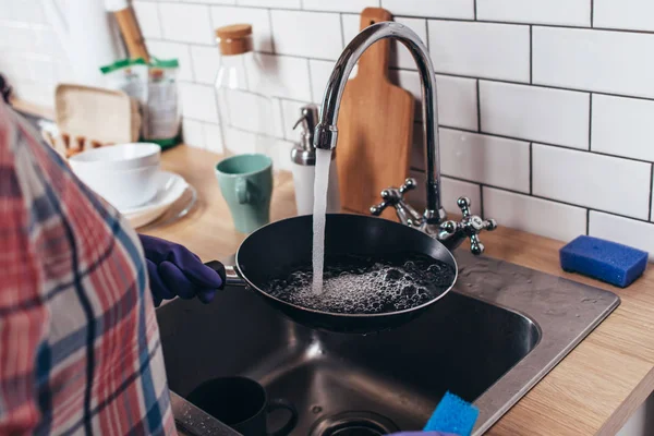 Jovem mulher usando luvas de borracha lavando frigideira na cozinha — Fotografia de Stock