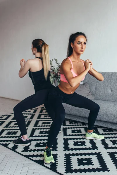 Due donne in forma che fanno squat a casa Allenamento femminile sport e fitness — Foto Stock