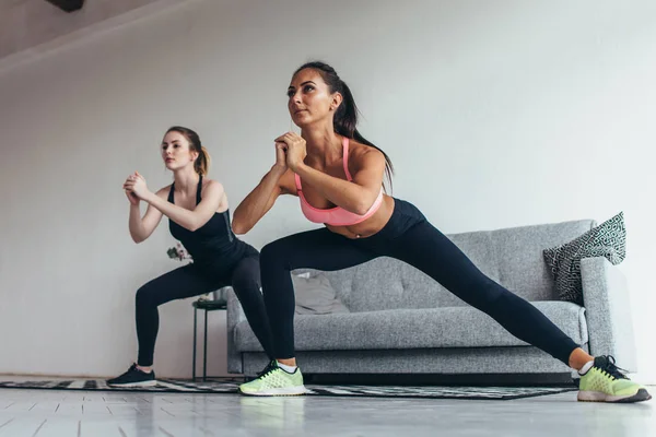 Duas meninas aptas a fazer exercícios em casa realizando lunges laterais em casa — Fotografia de Stock