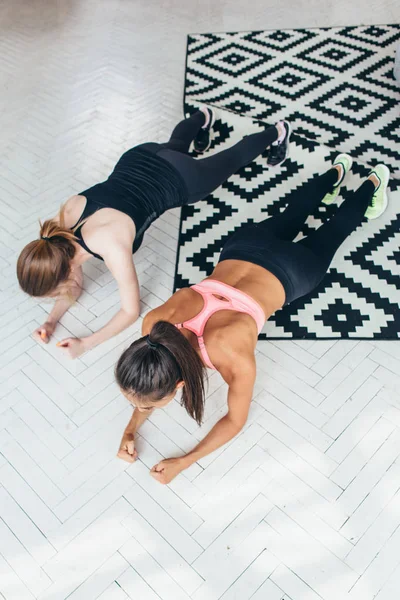 Dos mujeres en forma haciendo ejercicio de tablón en el suelo en casa Entrenamiento de espalda y músculos de prensa, deporte, entrenamiento de fitness —  Fotos de Stock