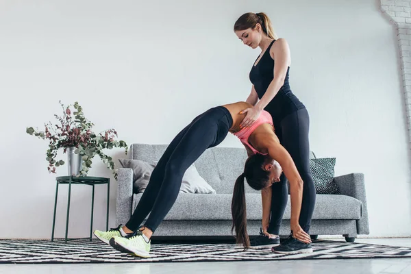 Fit woman making arching back with the help of personal trainer supporting her.
