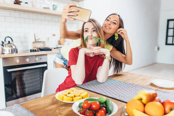 Mujeres preparando comida jugando con verduras en la cocina divirtiéndose y tomando selfie . — Foto de Stock