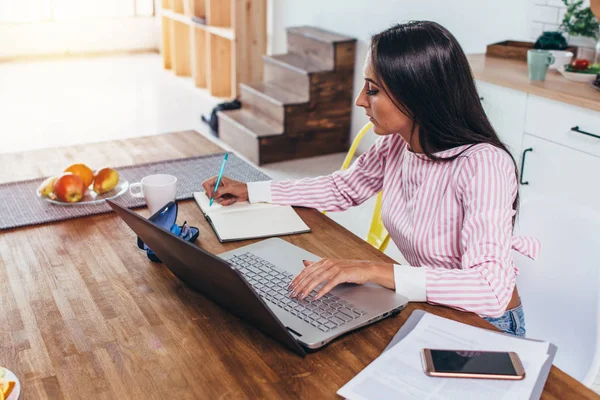 Koncentrerad freelancer kvinna att göra anteckningar från internet arbetande hem sittande vid bord — Stockfoto