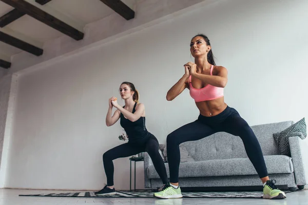 Twee passen vrouwen doen squats op home vrouwelijke training sport en fitness. — Stockfoto