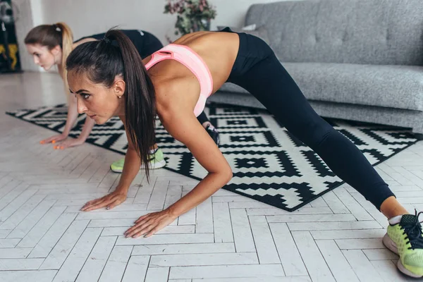 Dos chicas en forma haciendo ejercicios en casa realizando embestidas laterales en casa . — Foto de Stock