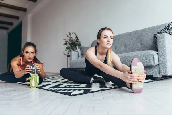 Přizpůsobit ženy dělají, strečink, zatímco sedí na podlaze doma — Stock fotografie