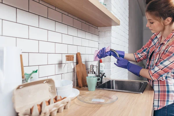 Mujer joven con fregadero de limpieza de guantes, limpiando el grifo en la cocina — Foto de Stock