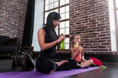 Genç beyaz bir kadın ve mat bacaklar ile oturup yoga eğitim içme suyu geçtikten sonra rahatlatıcı, muz yemek spor stüdyosunda bir mutlu kız çocuğu
