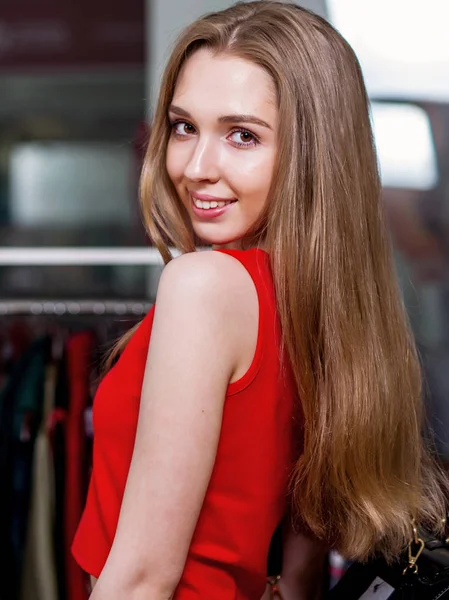 Porträt eines Models in rotem Kleid mit langen blonden Haaren, das in einem Einkaufszentrum zurückblickt — Stockfoto