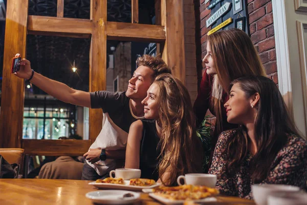 Amigos emocionados tomando selfie con teléfono inteligente sentado en la mesa teniendo una salida nocturna . — Foto de Stock