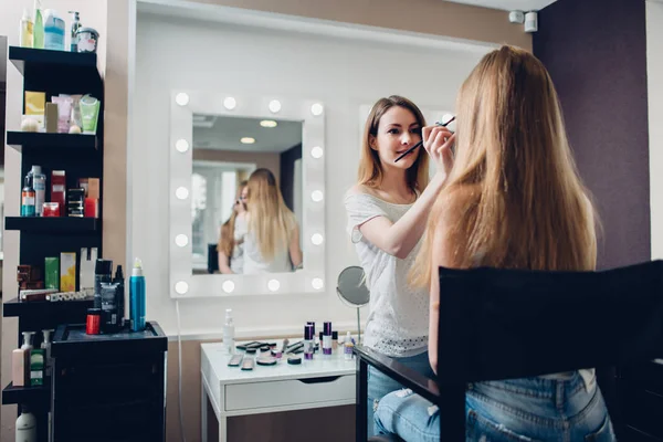 Esteticista feminina sorridente aplicando maquiagem usando escova para o modelo feminino no estúdio de beleza elegante — Fotografia de Stock