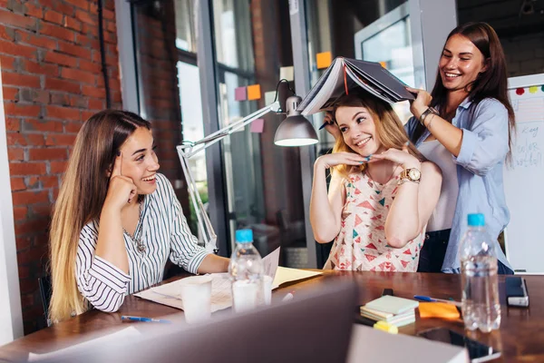 Three funny young students having fun while sitting at desk preparing for exam in study room — Stock Photo, Image