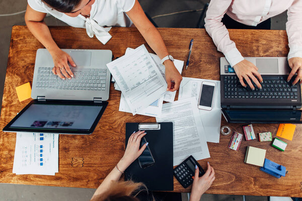 Top view of three women working with documents using laptops sitting at desk