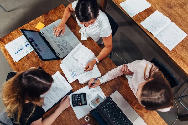 Equipo de mujeres contadoras preparando informe financiero anual trabajando con papeles usando computadoras portátiles sentadas en el escritorio en la oficina — Foto de Stock