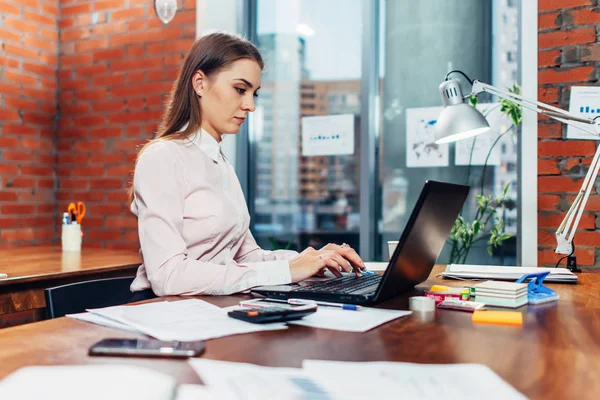 Jovem mulher vestindo roupas formais trabalhando em laptop digitando e-mails sentados em seu local de trabalho — Fotografia de Stock