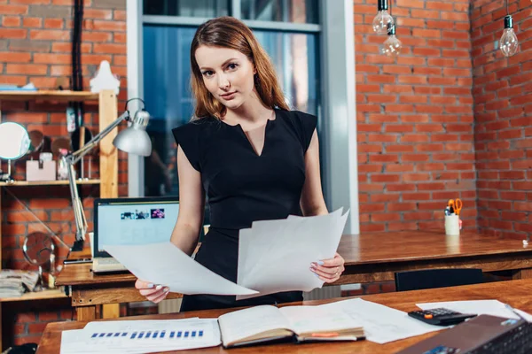 Serious woman reading papers studying resumes standing at work desk in stylish office — Stock Photo, Image