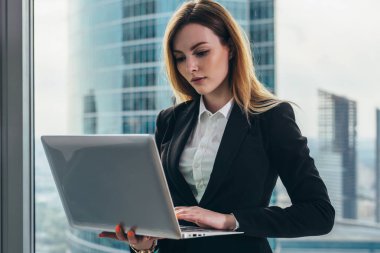 İş bölgesi manzaralı panoramik pencere karşı bir laptop ayakta tutan lüks ofisinde çalışan genç kadın avukat