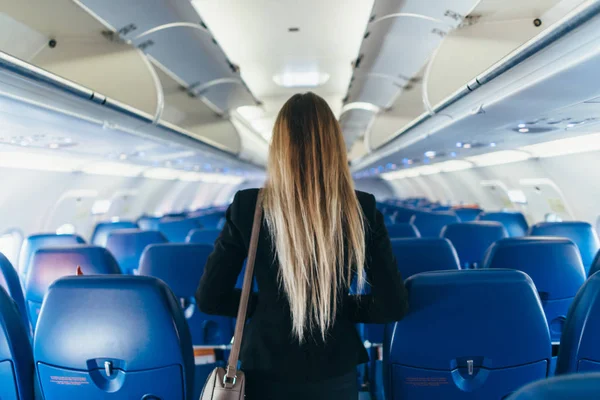 Vista trasera de la joven mujer vestida con traje formal caminando por el pasillo en avión —  Fotos de Stock