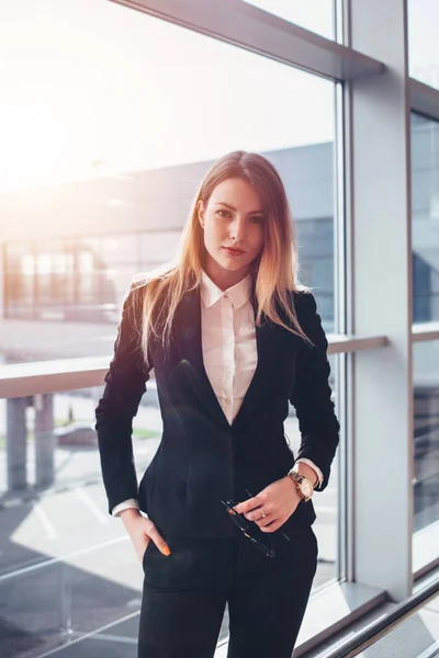 Portrait of attractive blonde wearing elegant formal suit standing in airport terminal — Stock Photo, Image