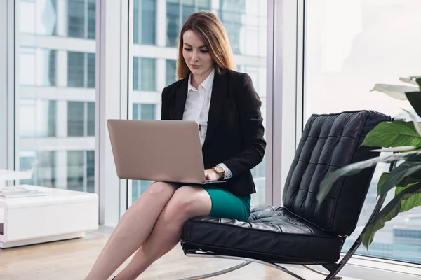 Chefökonomin analysiert Daten mit Laptop im Sessel im modernen Büro — Stockfoto