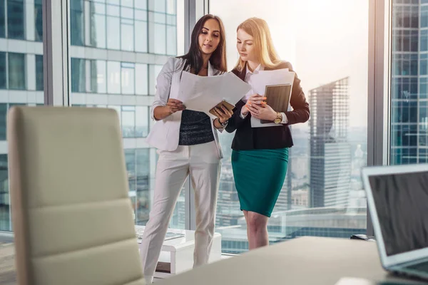 Donne d'affari che indossano abiti formali discutono documenti in piedi nel corridoio ufficio — Foto Stock