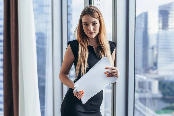 Porträt einer hübschen jungen Frau, die im Büro Dokumente in die Kamera hält — Stockfoto