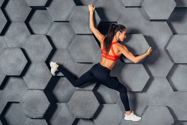 Fit woman posing like a climber hanging on decorative wall — Stock Photo, Image