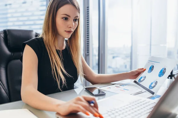 Direttore donna che lavora in ufficio seduto alla scrivania analizzando le statistiche aziendali in possesso di diagrammi e grafici utilizzando laptop — Foto Stock