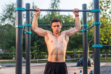 Parkta barfiks egzersizi yapan genç bir erkek atlet. Fitness adamı dışarıda çalışıyor.